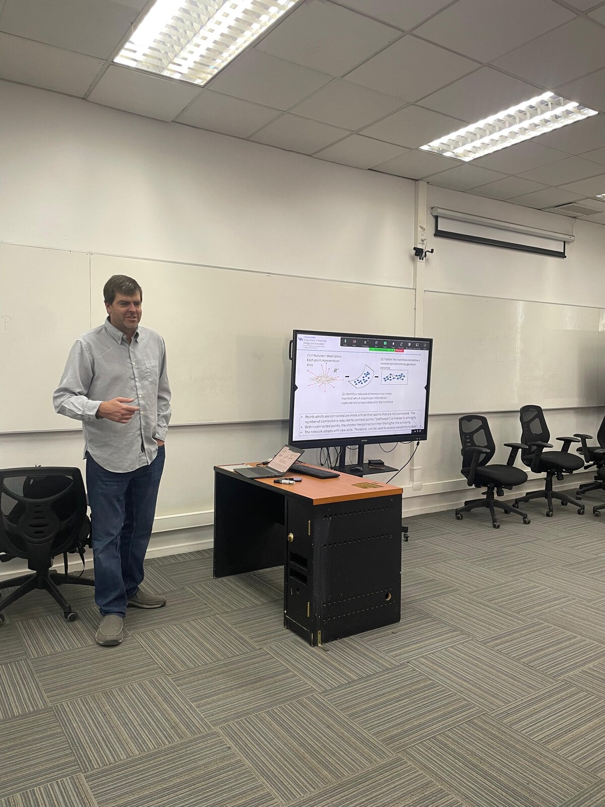 Scott Broderick explicando junto a una pantalla con la presentación de la primera clase